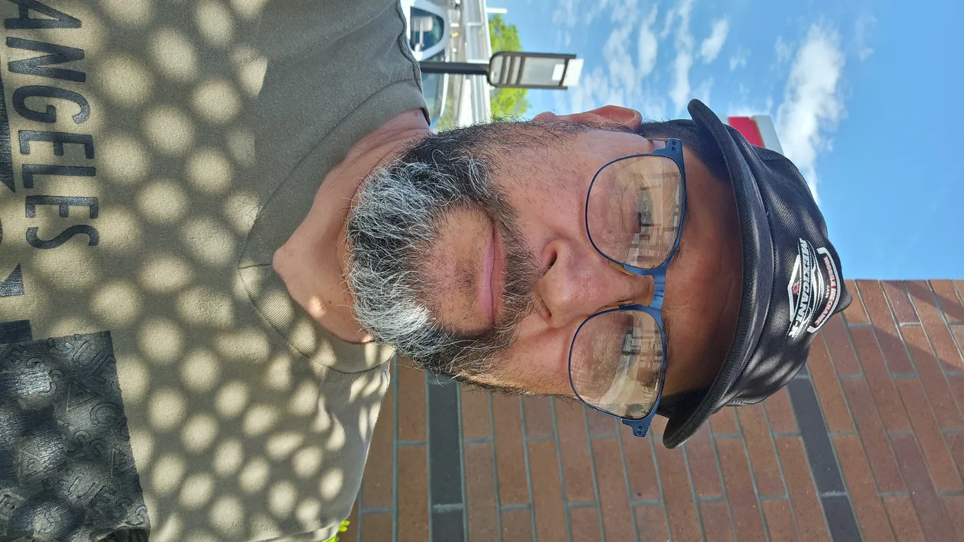 Man with glasses and cap beside brick wall in Concord, NC.